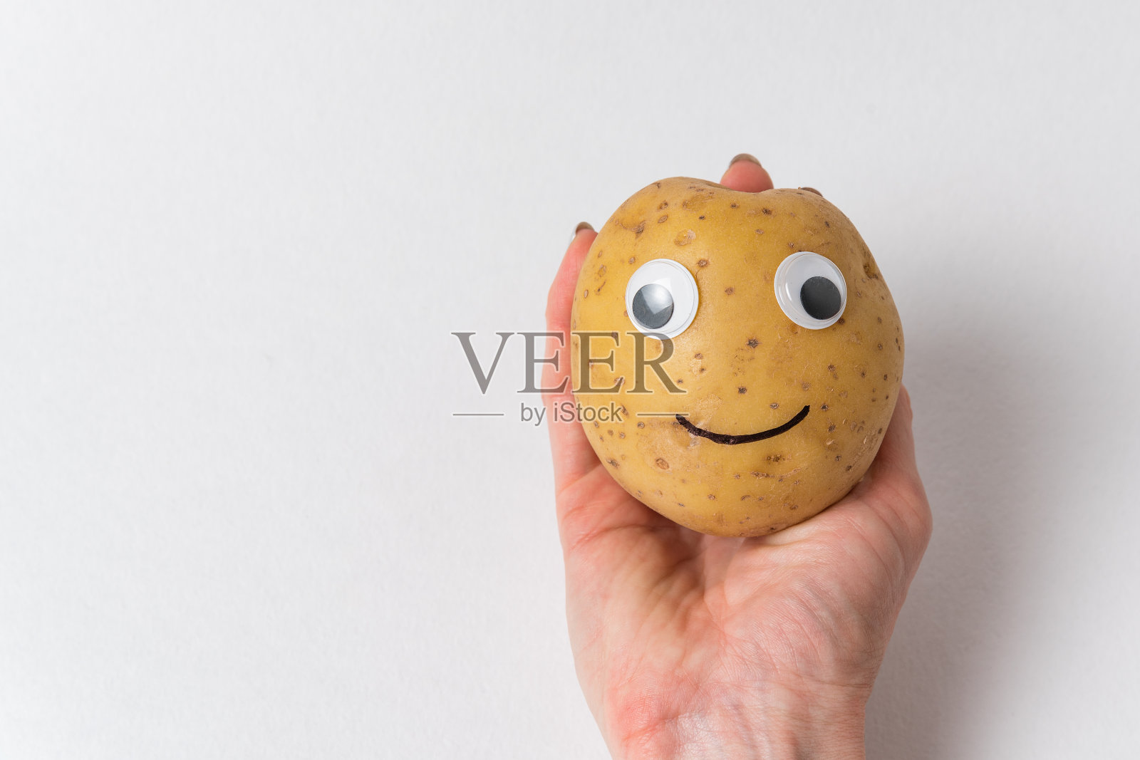 白色背景上的手画上了带有眼睛和微笑的搞笑土豆。照片摄影图片