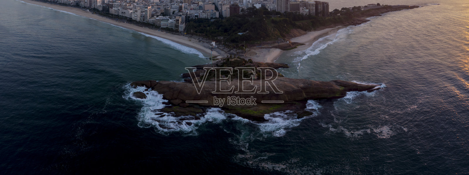 在巴西里约热内卢的Arpoador岩石上旋转的海浪图案，以伊帕内玛海滩和更广阔的城市景观为背景，映衬着日出时五彩缤纷的天空照片摄影图片