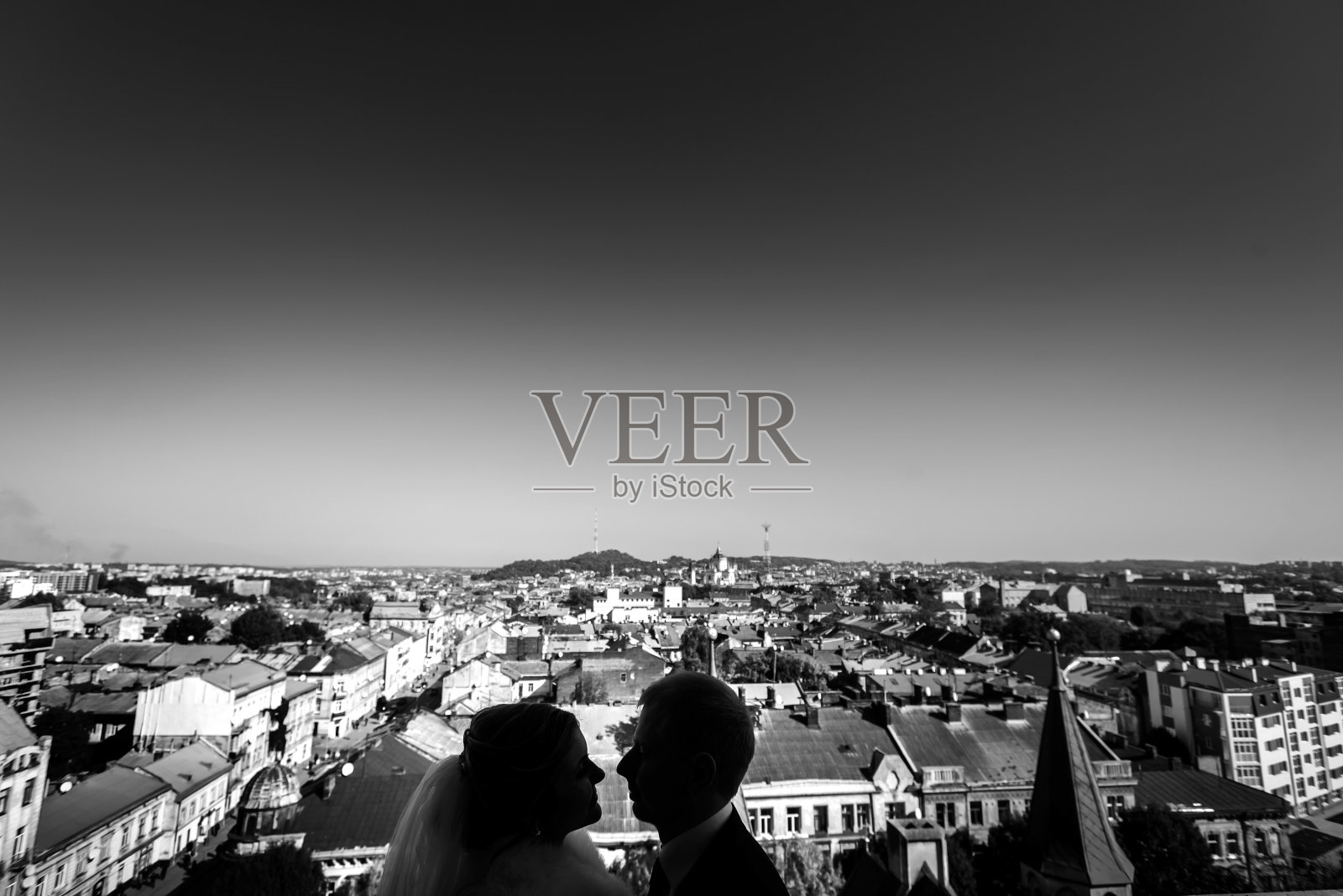 屋顶上的剪影是幸福的新娘和时尚的新郎抱在一起的真实情感，与古老的城市建筑和城市景观，黑白相间照片摄影图片