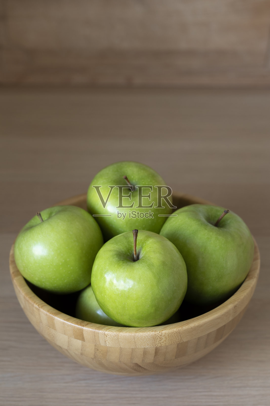 桌上的木碗里装着青苹果。照片摄影图片