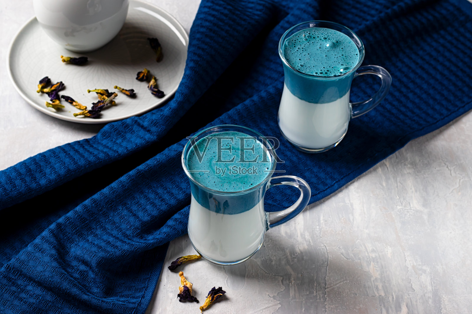 两杯蓝色达尔戈纳抹茶蓝色拿铁，淡灰色背景上的奶油豌豆蝴蝶饮料照片摄影图片