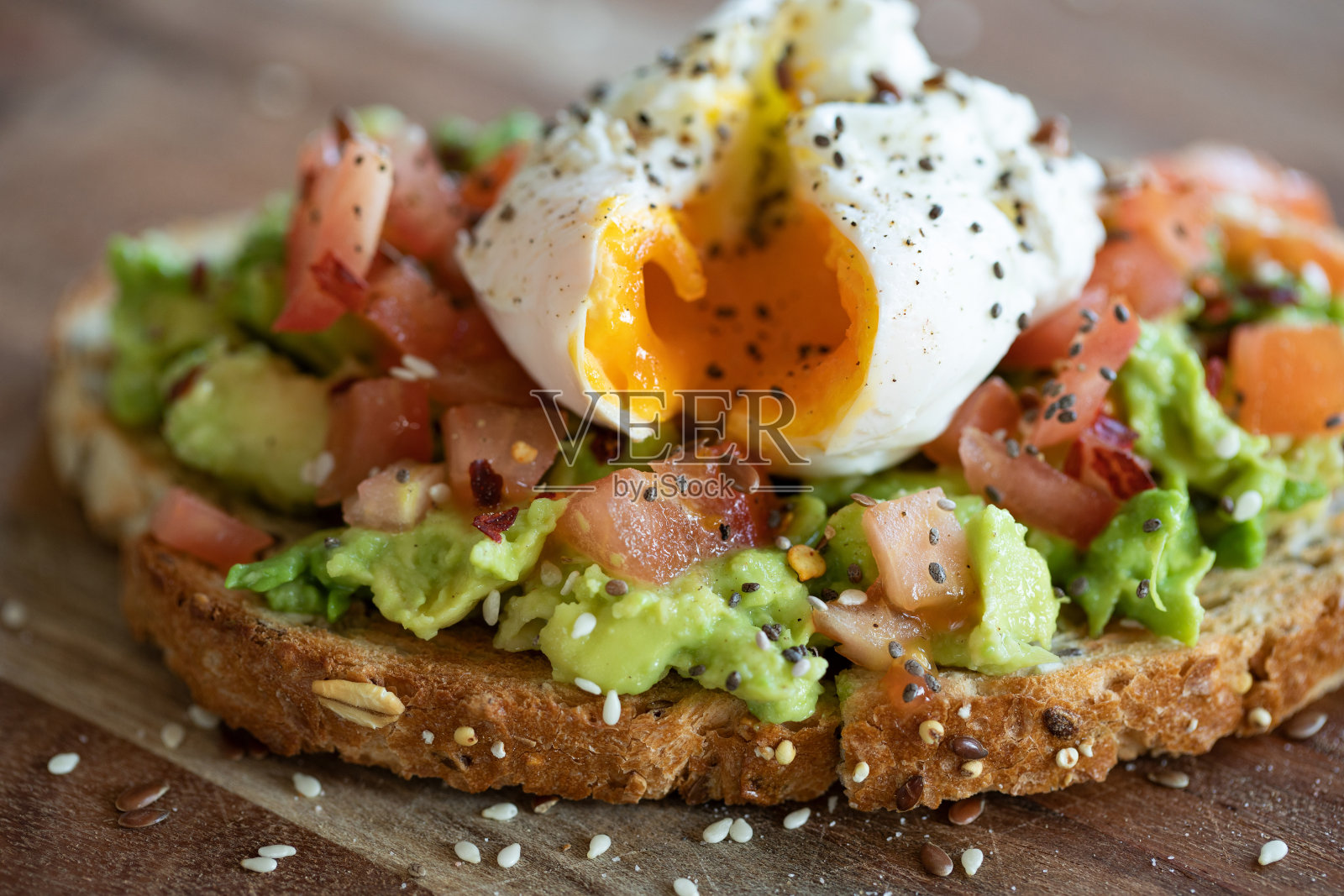 这是一顿健康的纯素食餐，木盘上的麦片烤面包片上撒着奇亚和芝麻，还有番茄丁和鳄梨。照片摄影图片