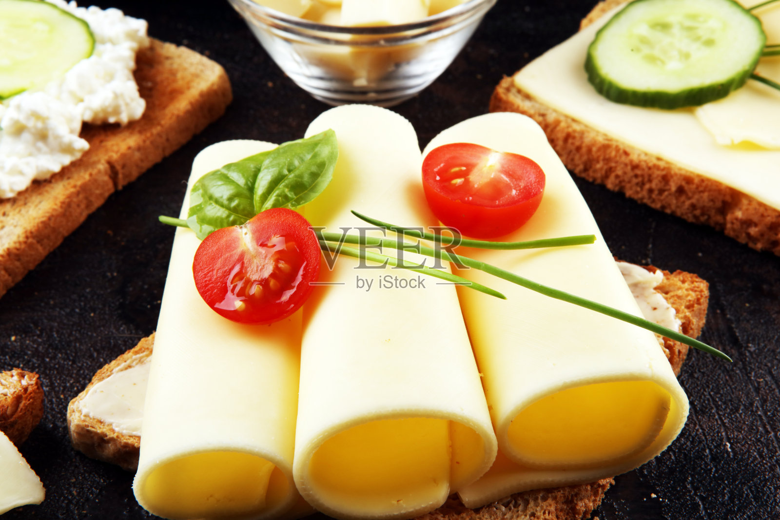 在三明治上用黄瓜片和香草装饰的金色豪达奶酪或奶油奶酪卷成的薄片。早餐吃面包或烤面包加奶酪照片摄影图片