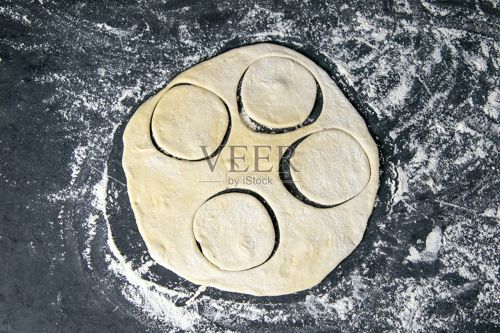 在黑色背景下从面团上切圆的过程。前视图,特写照片摄影图片