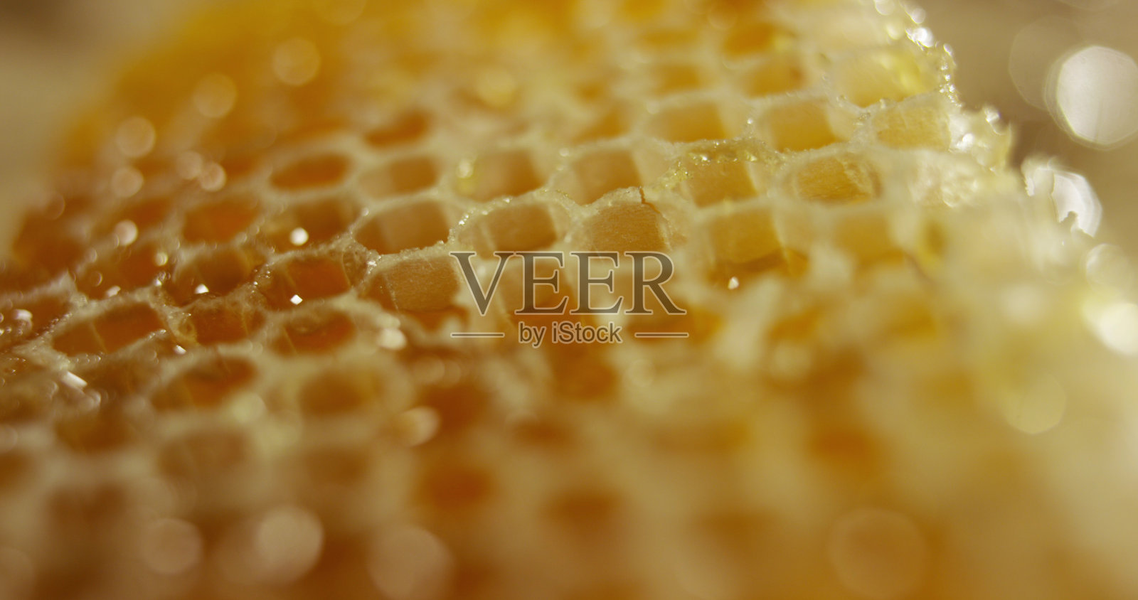 生物蜂蜜和真正的蜂蜜滴在一个罐子里。蜂房滴蜜。黑色的背景和一张木桌。照片摄影图片