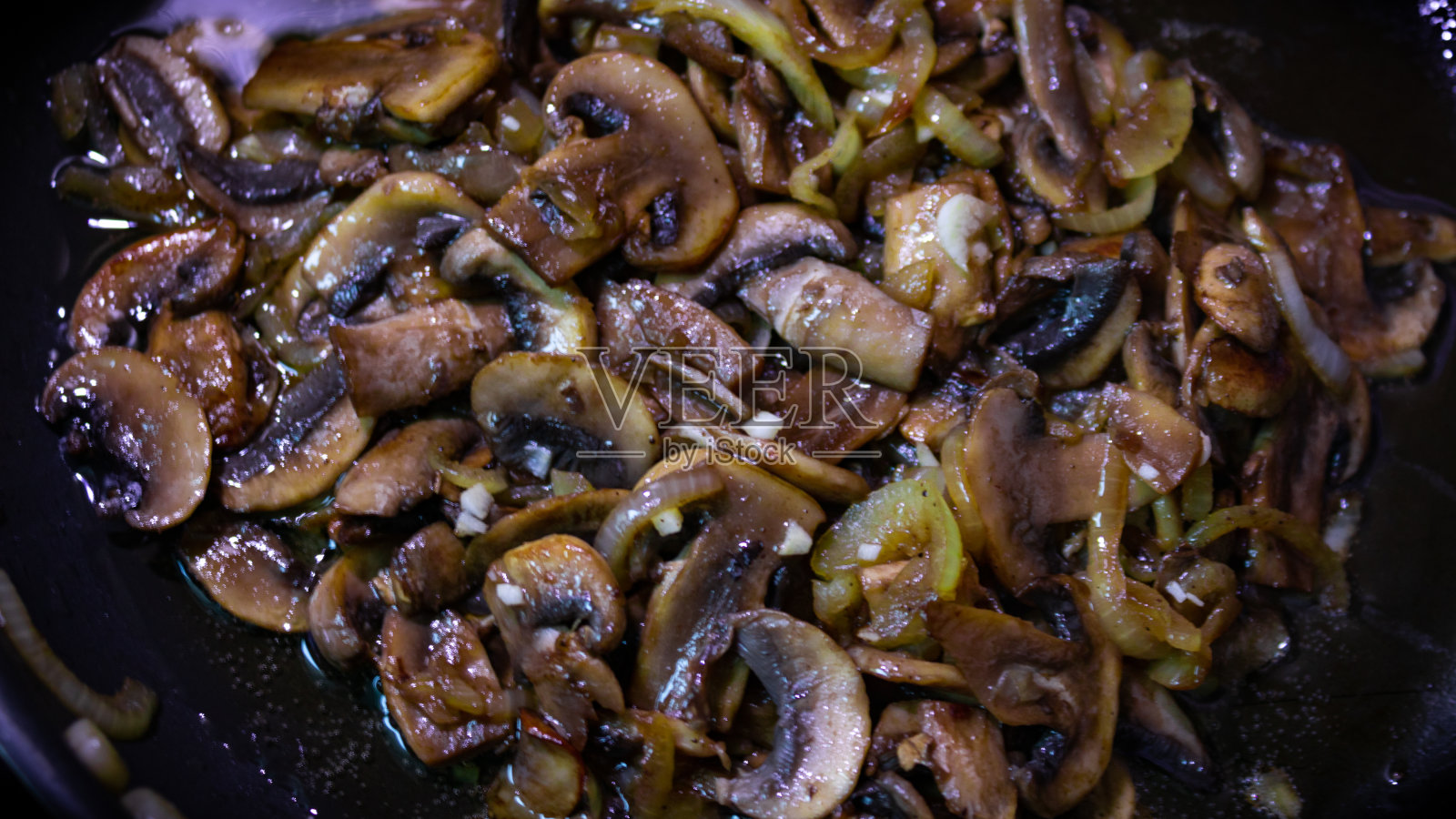 用平底锅将新鲜蘑菇和洋葱切成片。用热锅煎蘑菇。照片摄影图片