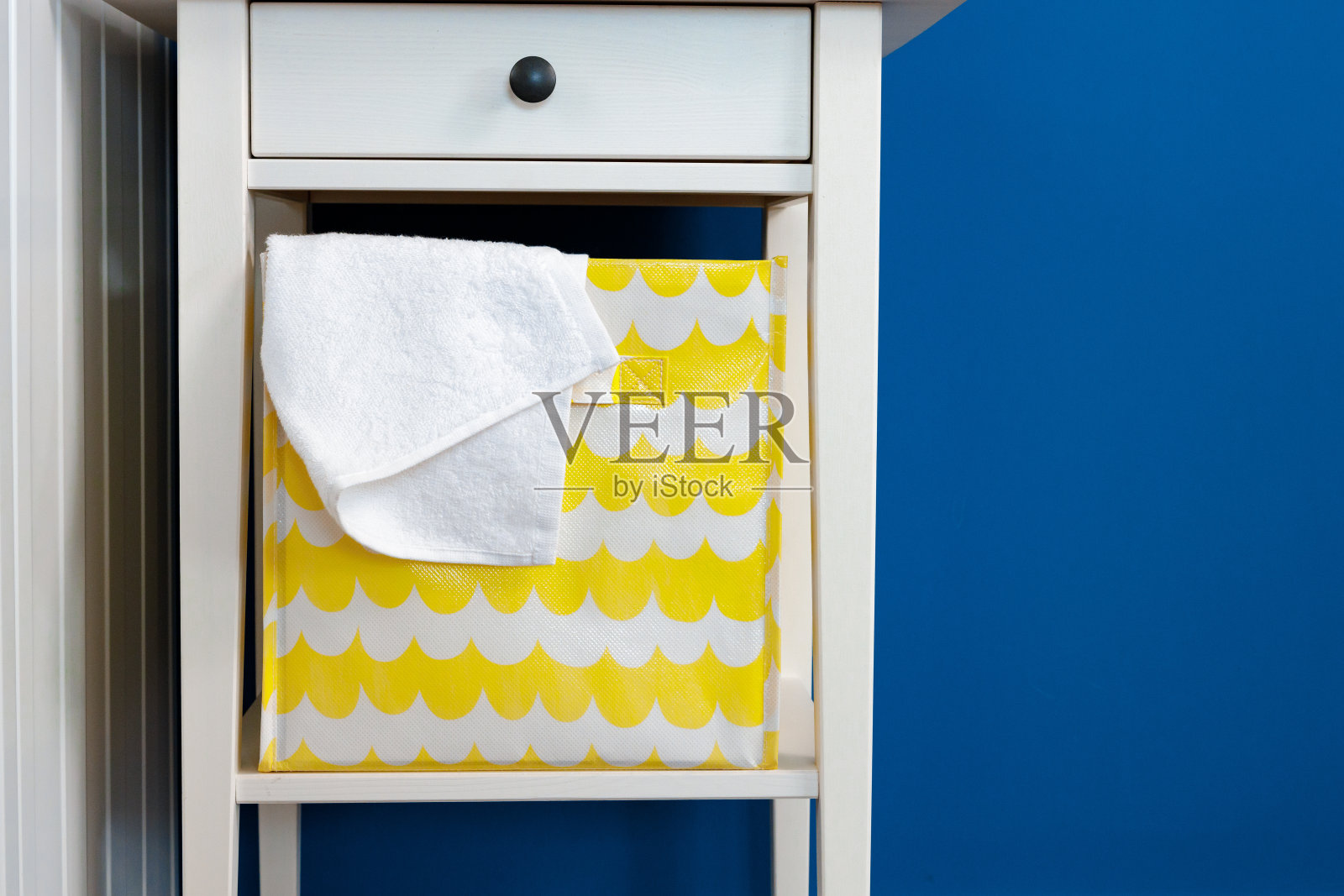 白色木质床头柜和储物箱靠在蓝色的墙上照片摄影图片