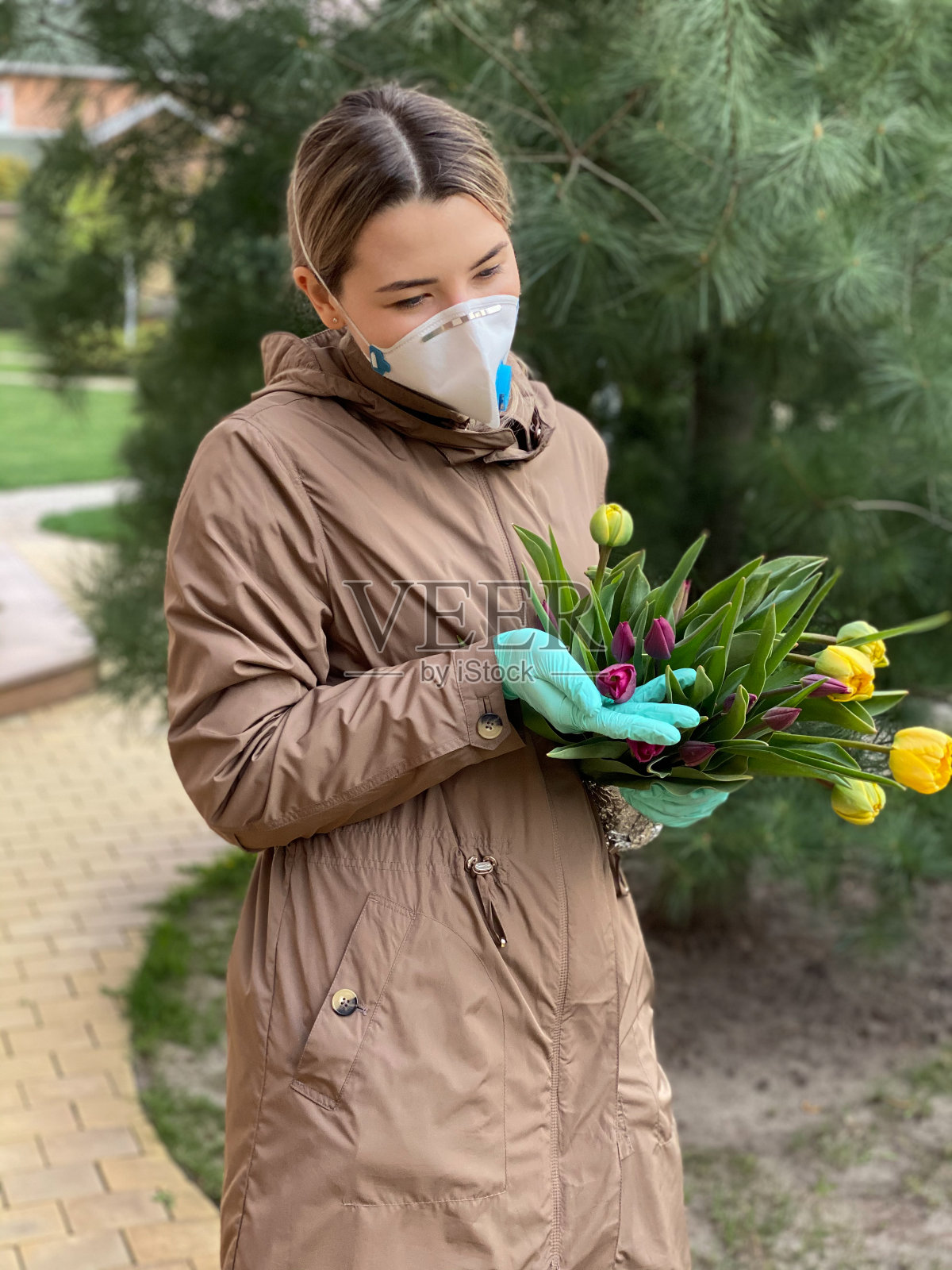 年轻女子在户外戴着防护面具和手套，手持一束鲜花。新型冠状病毒肺炎美丽的女孩戴着医用口罩抗击自然界的冠状病毒。照片摄影图片