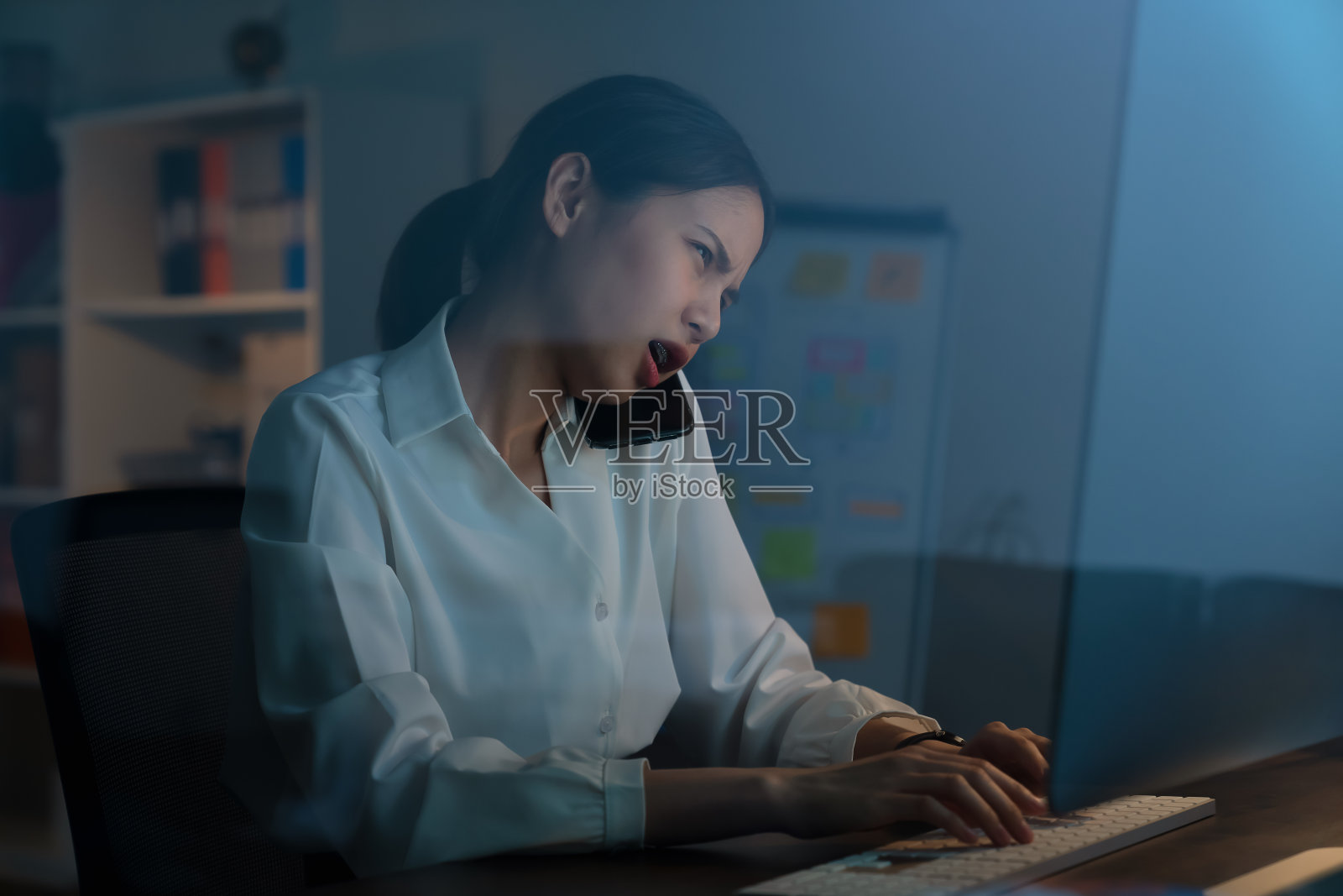 由于工作紧急，疲惫的亚洲女商人在晚上讲电话和工作电脑。照片摄影图片