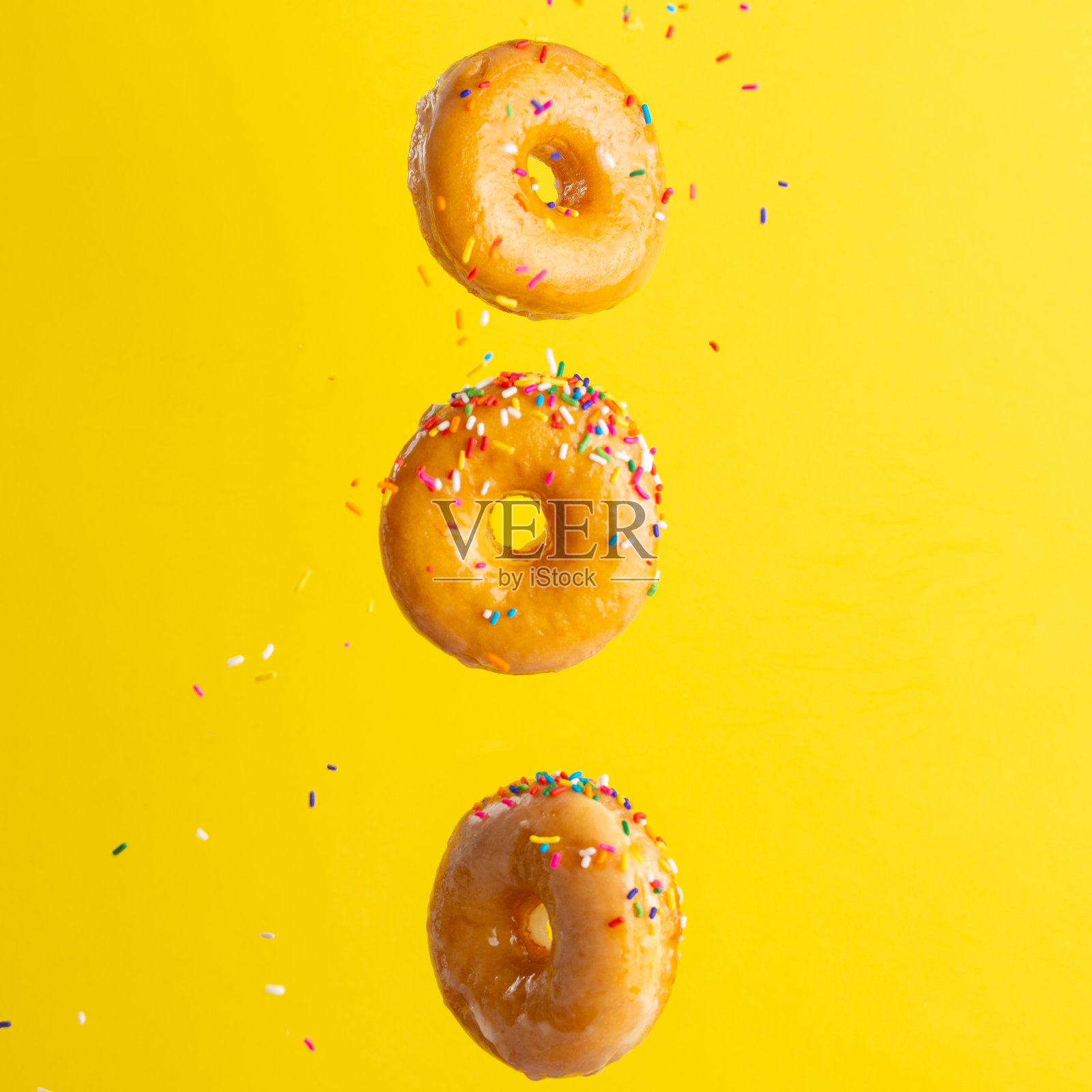 甜甜圈飞行。很多甜甜圈都是彩色的焦糖，黄色的背景上还撒有糖屑。垂直的照片。冻结。照片摄影图片