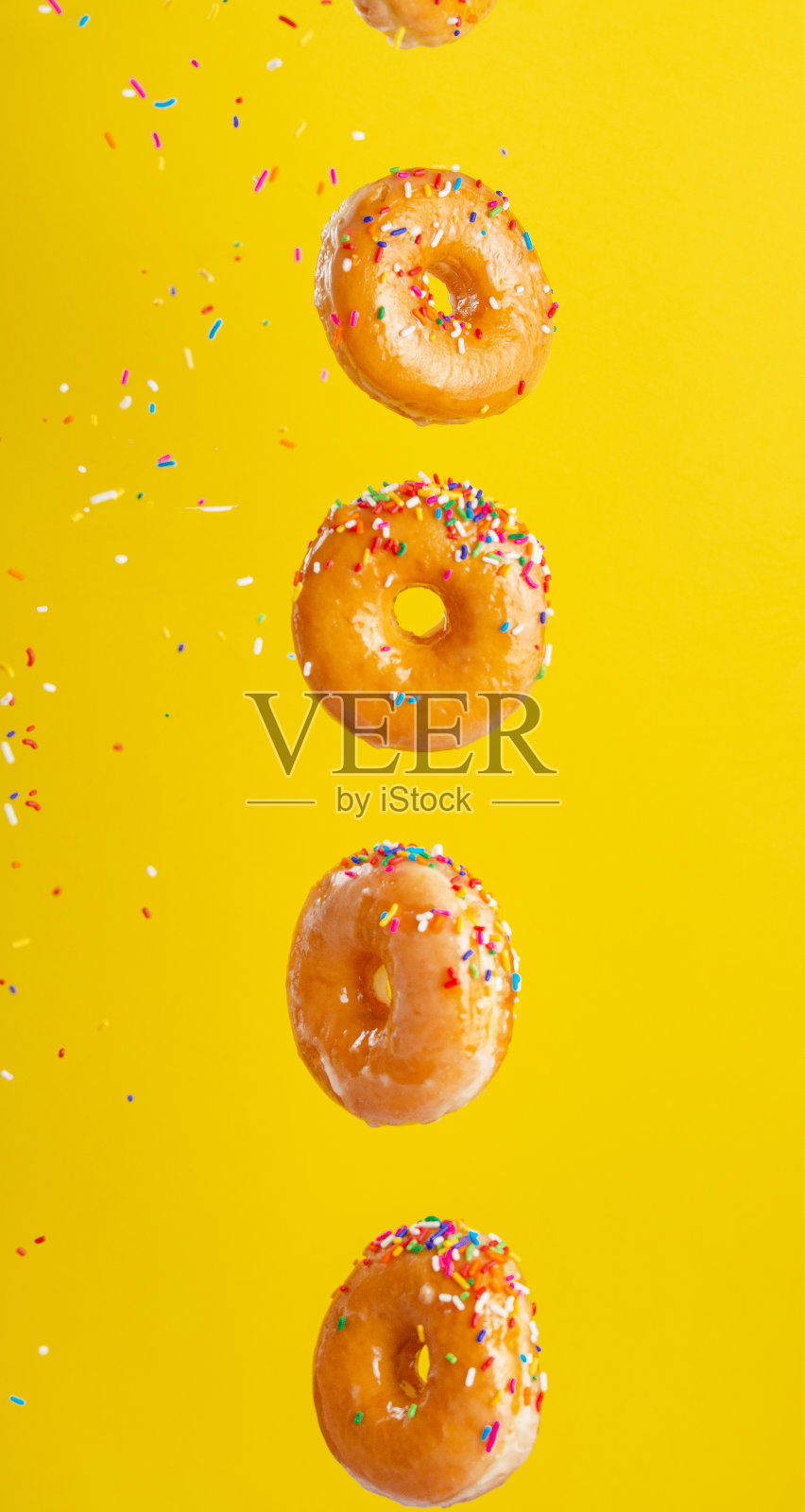 各种装饰的甜甜圈在运动落在黄色的背景。甜的和冰的甜甜圈落下或飞在运动中。焦糖。黄色背景，垂直照片。照片摄影图片