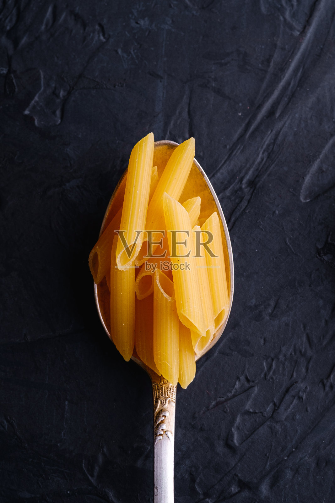 刀叉勺与cavatappi生的金色小麦卷面食在深色纹理的背景，俯视图照片摄影图片