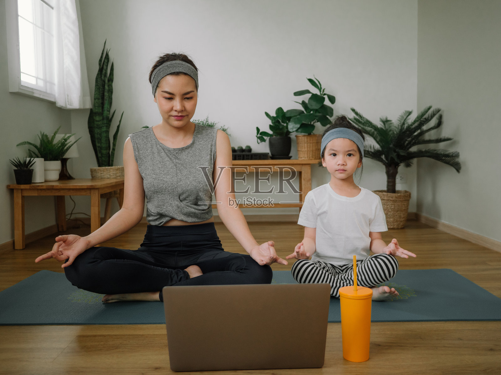 年轻的母亲和女儿在家里做练习。照片摄影图片