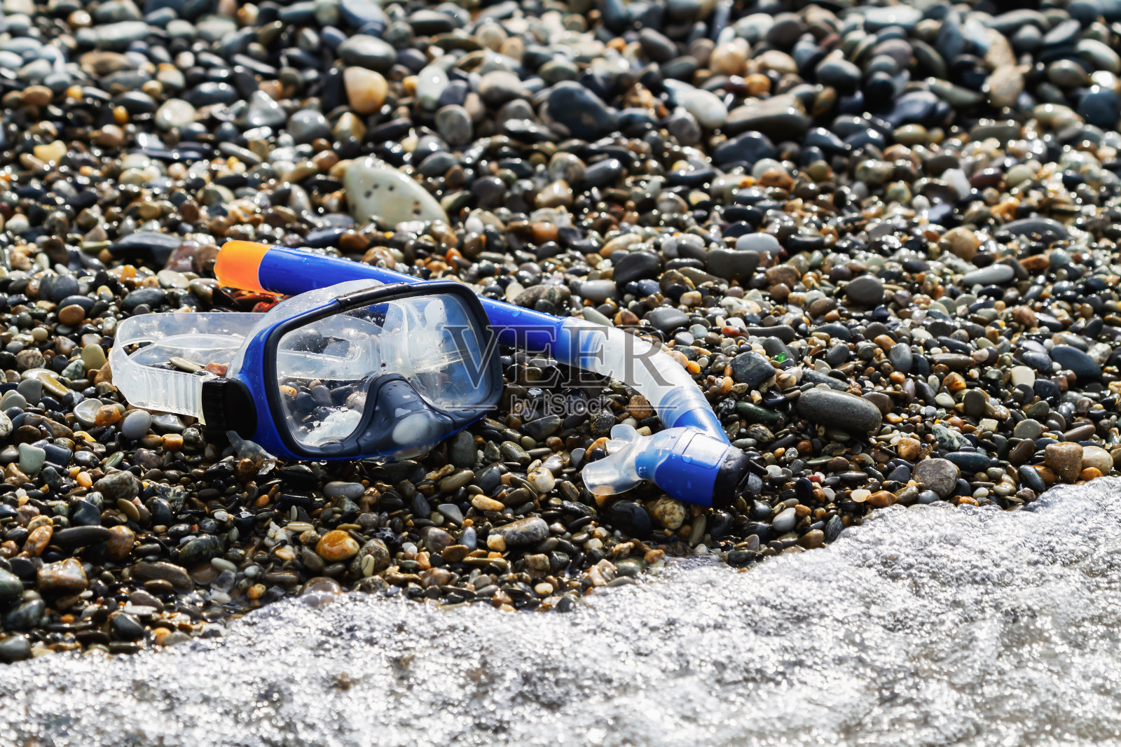 在卵石滩上潜水用的蓝色通气管和面罩照片摄影图片