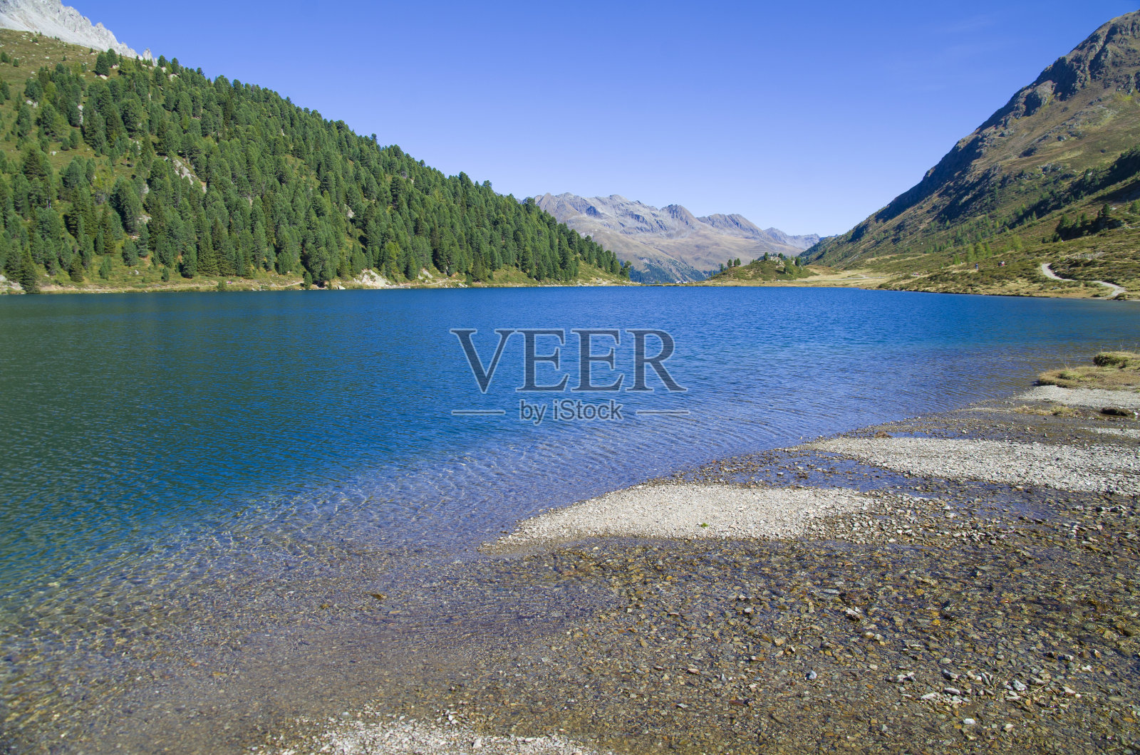 湛蓝的山湖在蓝天下，有树林、石头和雪照片摄影图片