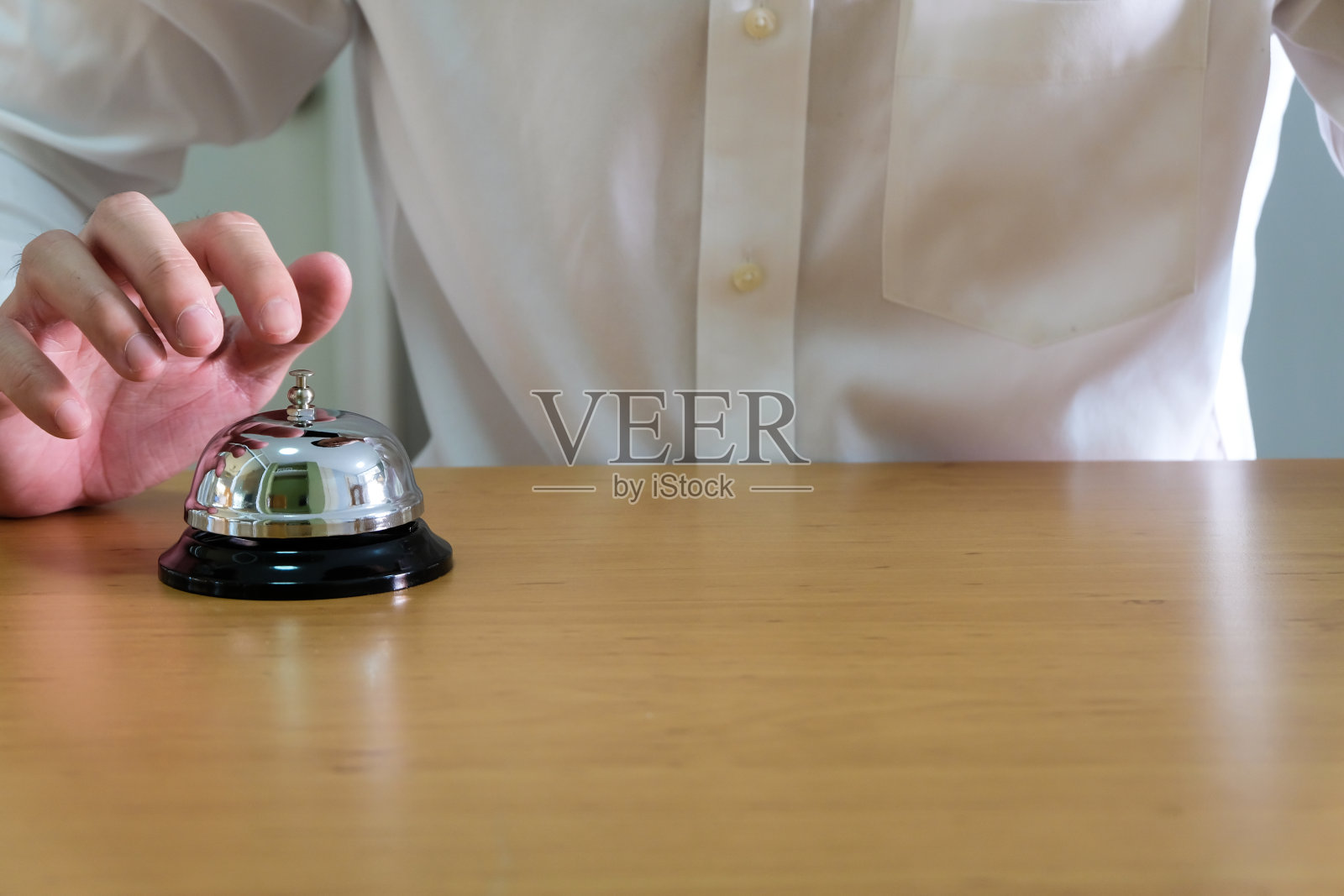 穿着白衬衫的男子伸手和手指按一下木质柜台上的接待或餐厅的铃，要求服务。酒店餐饮商务服务活动。照片摄影图片