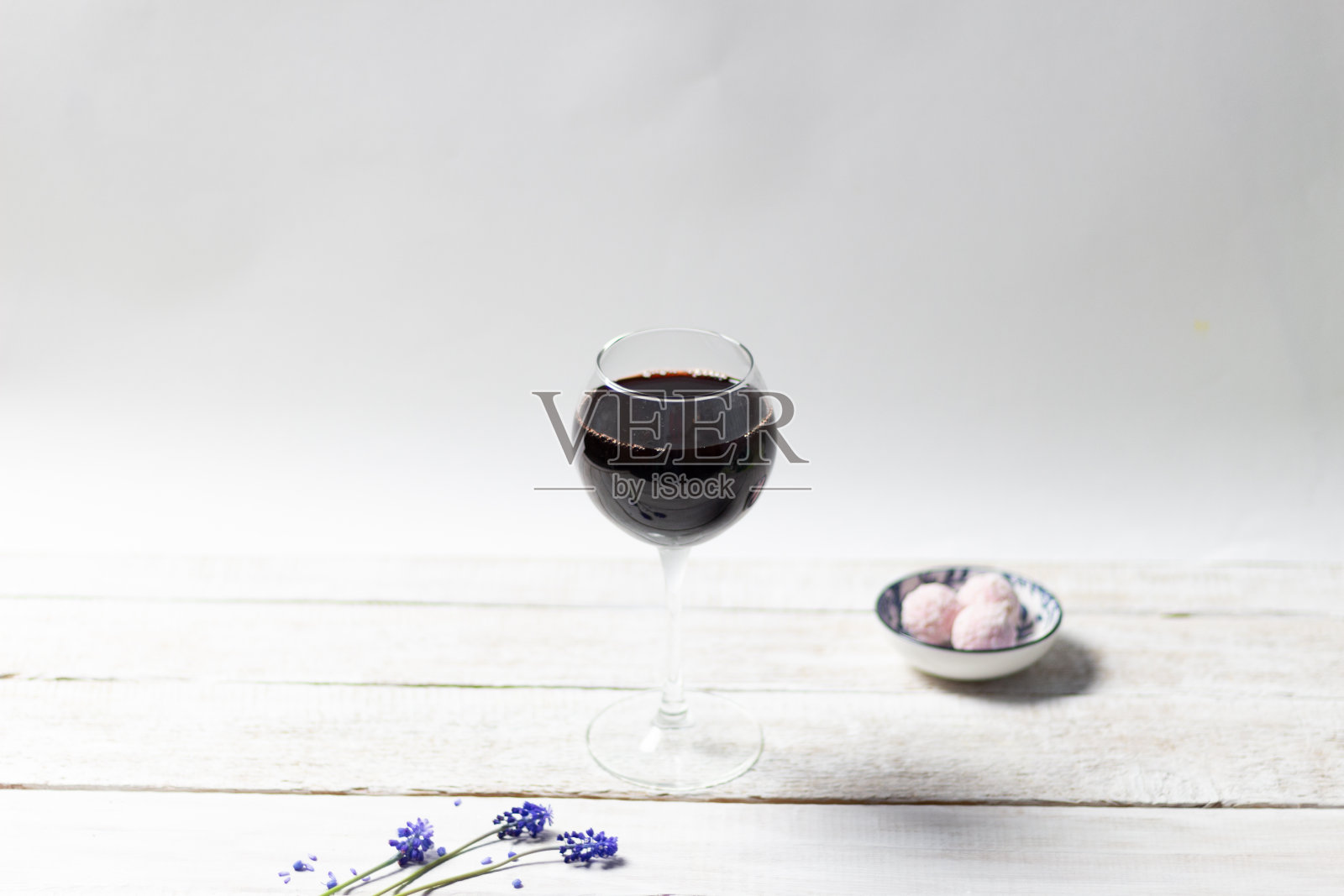 一杯红酒，白色的木质背景，蓝色的花朵和粉红色的圆糖果照片摄影图片