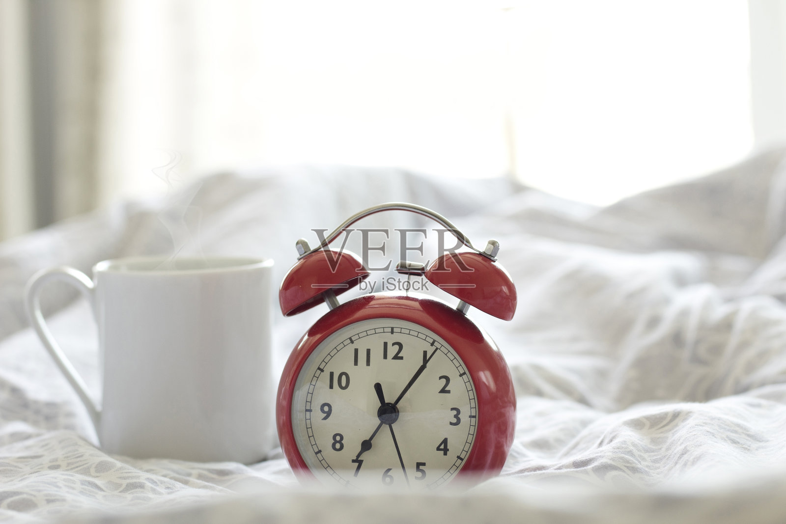 特写-闹钟有一个美好的一天与一杯咖啡在床上的背景在早晨的阳光。照片摄影图片