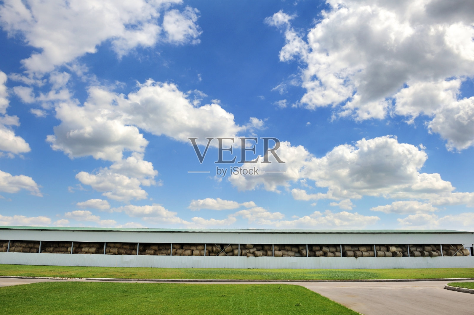 大机库储存干草在绿色的草地上，天空下美丽的云彩。照片摄影图片