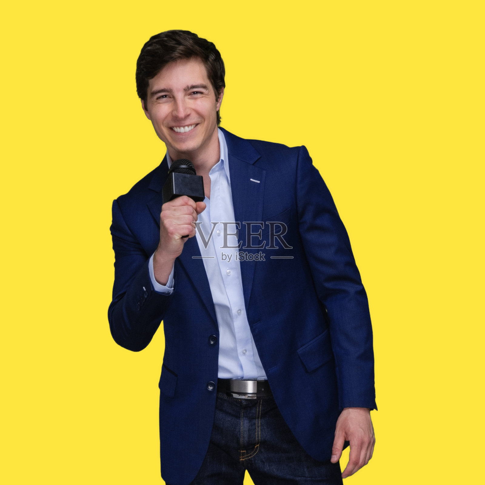 白人年轻男性演讲者站在黄色背景前，穿着衬衫，手持麦克风照片摄影图片