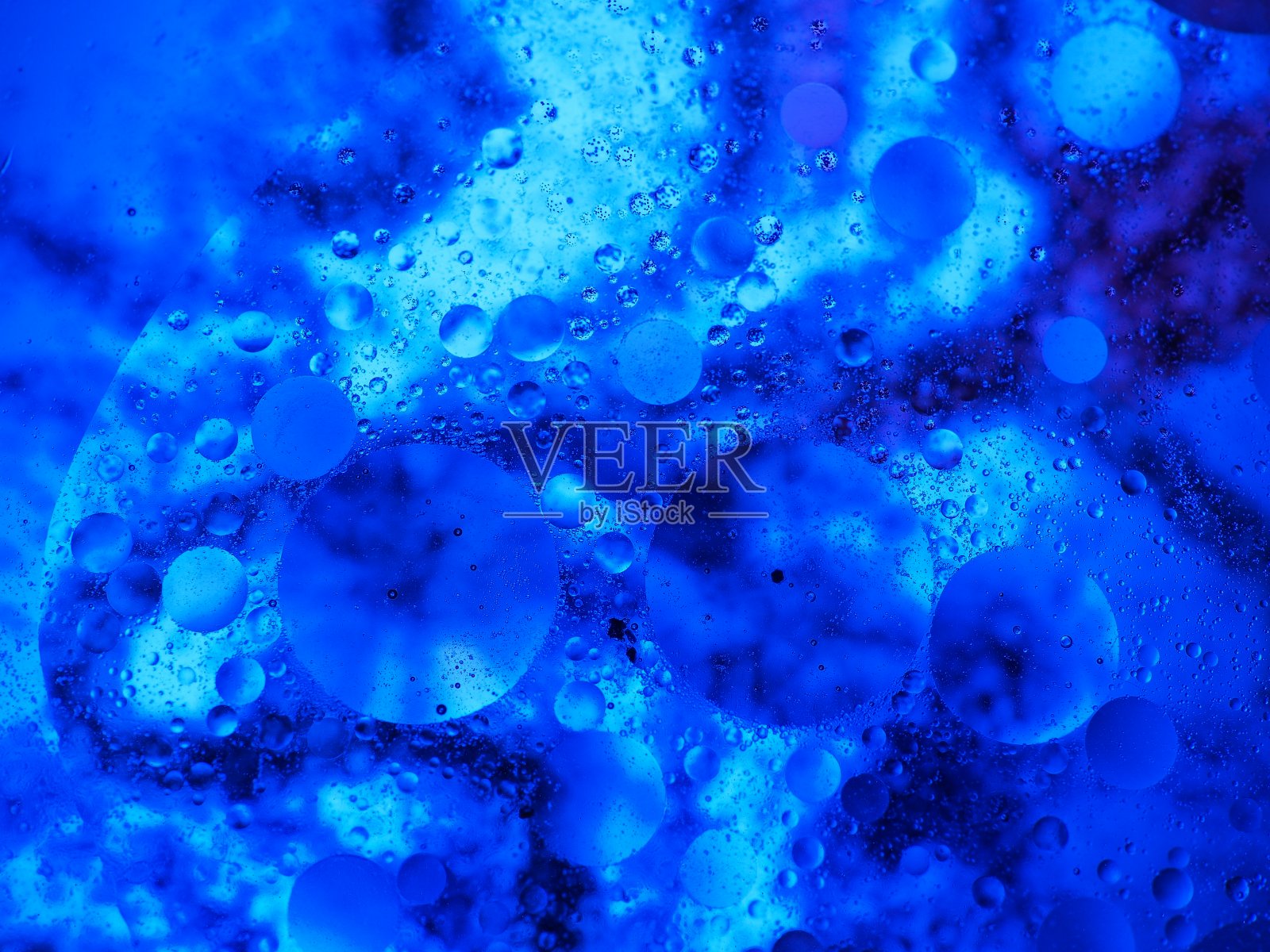 混合水和油，美丽的颜色。蓝色的光。特写镜头。抽象的宏观背景。水和油会起泡。摘要光照明照片摄影图片