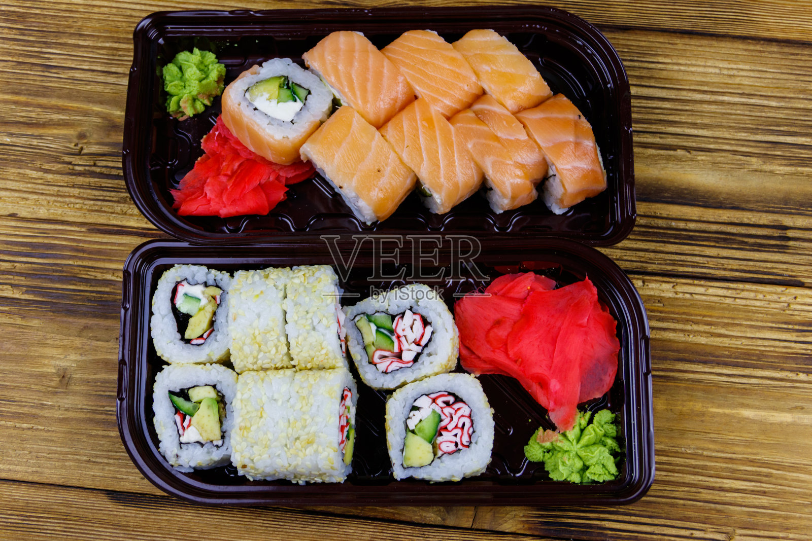 木桌上的塑料盒子里的寿司卷。前视图。装在塑料容器内的寿司供外卖或运送照片摄影图片