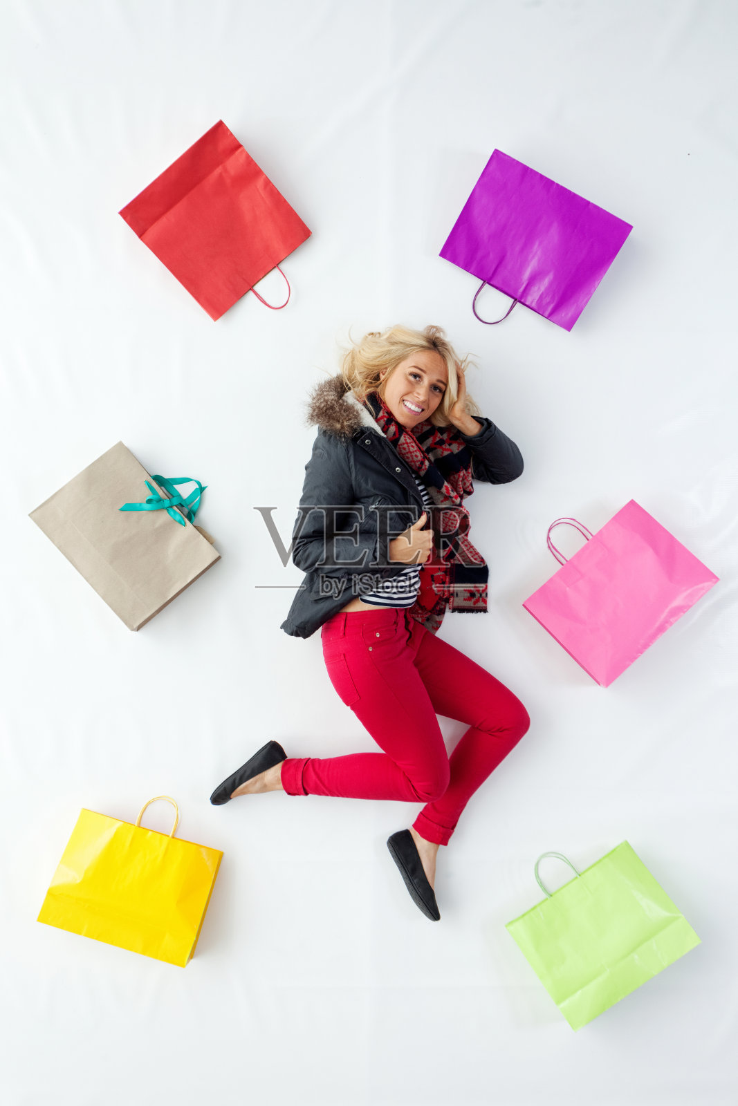 白种人年轻女性披着围巾，拿着购物袋，躺在白色背景前照片摄影图片