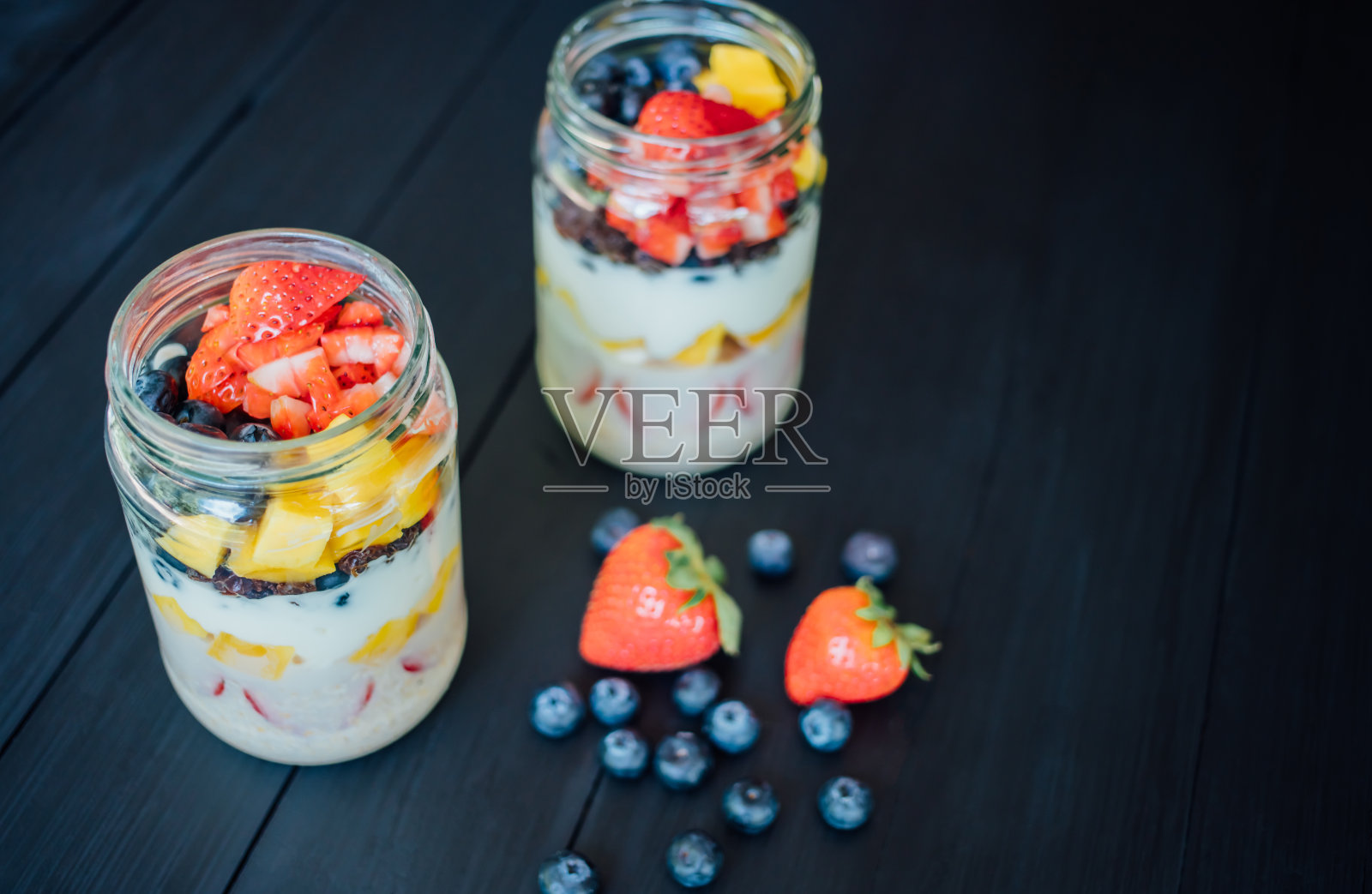 新鲜的芒果、蓝莓和草莓切片装在玻璃罐中，放在木桌上。早餐或健康食品概念，俯视图照片照片摄影图片