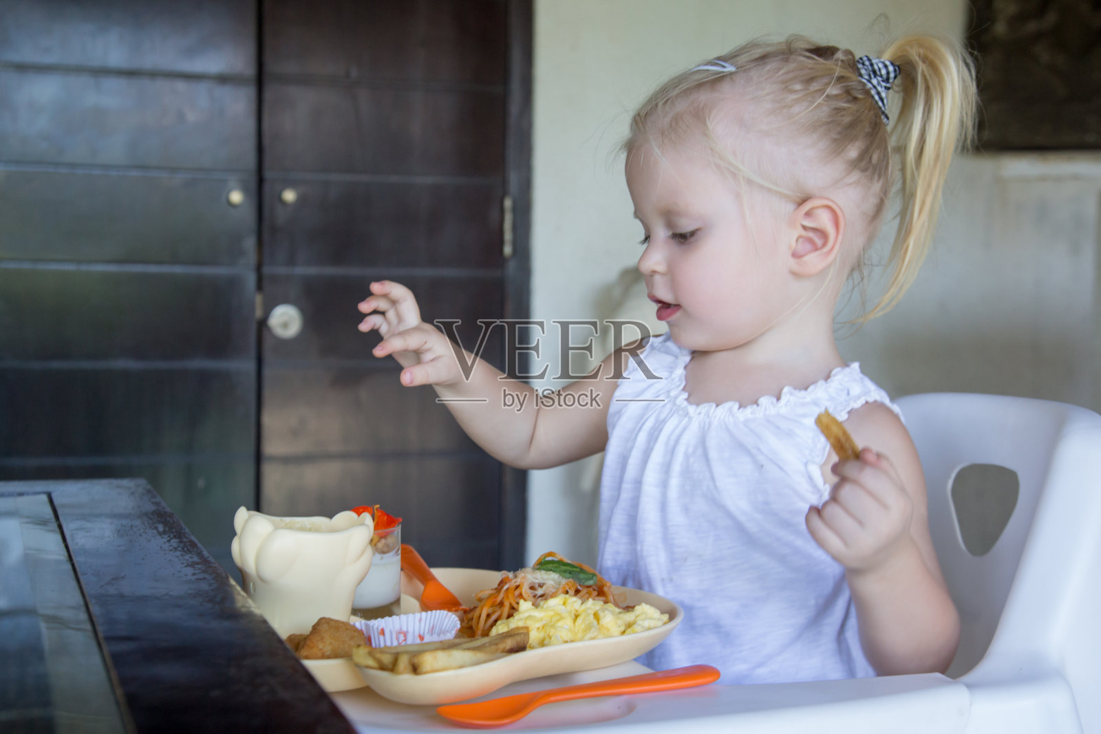 小女孩坐在厨房的高椅子上吃饭照片摄影图片