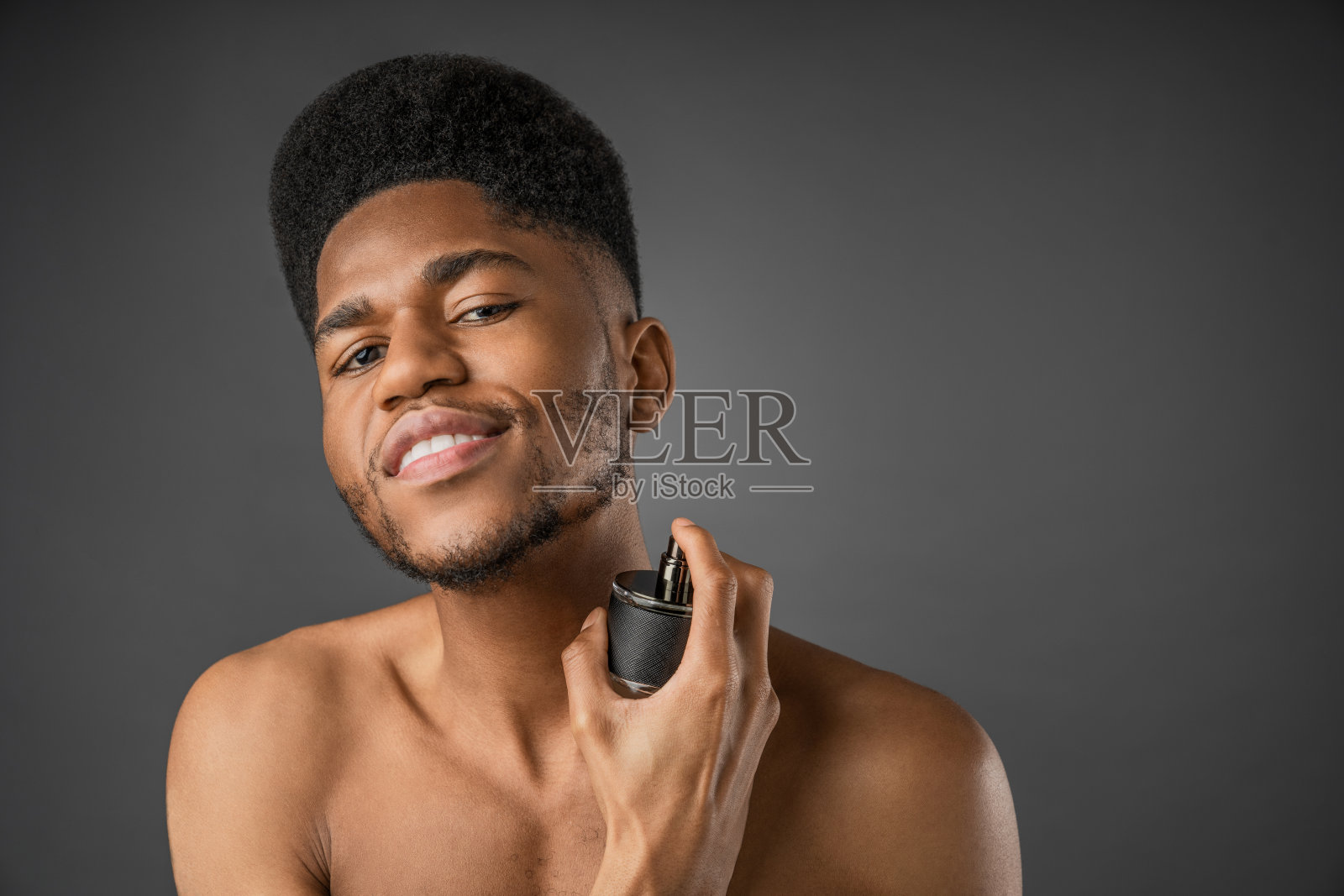 赤膊青年男子的肖像站在灰色背景和使用香水照片摄影图片