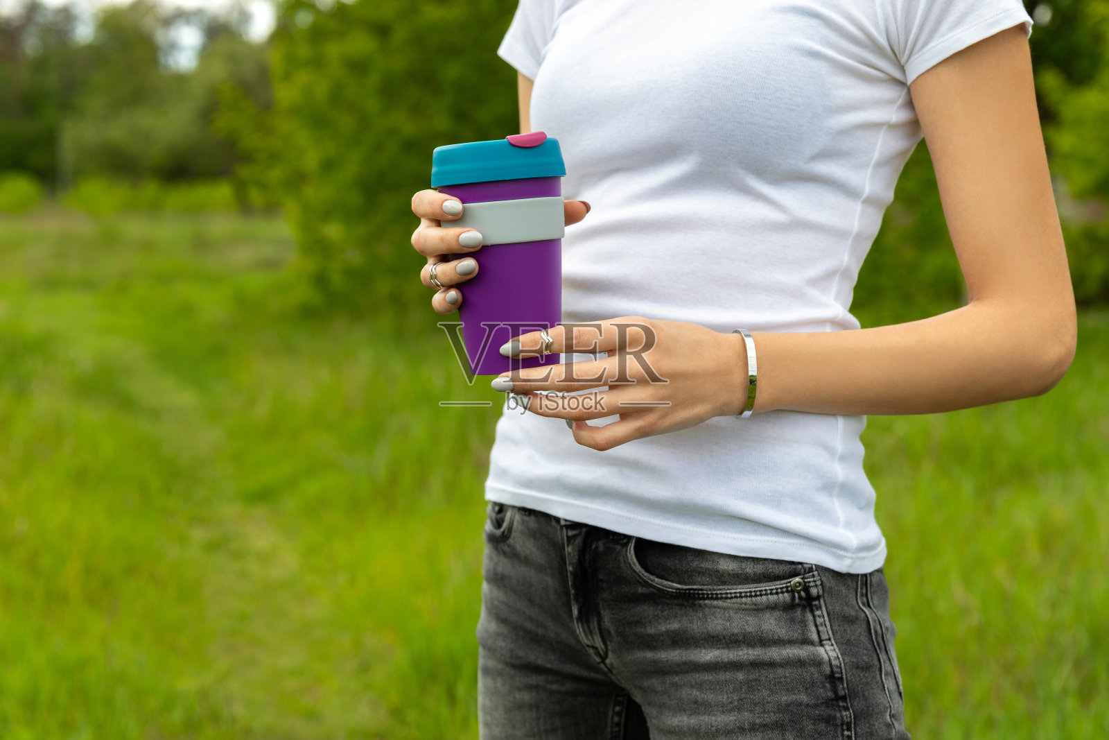 年轻的成年美丽的女人站在户外花园拿着一个可重复使用的热饮料杯照片摄影图片