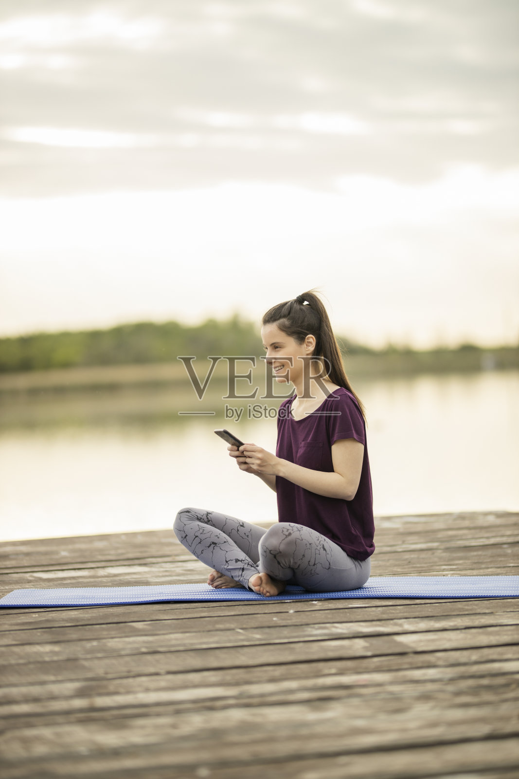 运动女性使用手机和坐在湖码头照片摄影图片