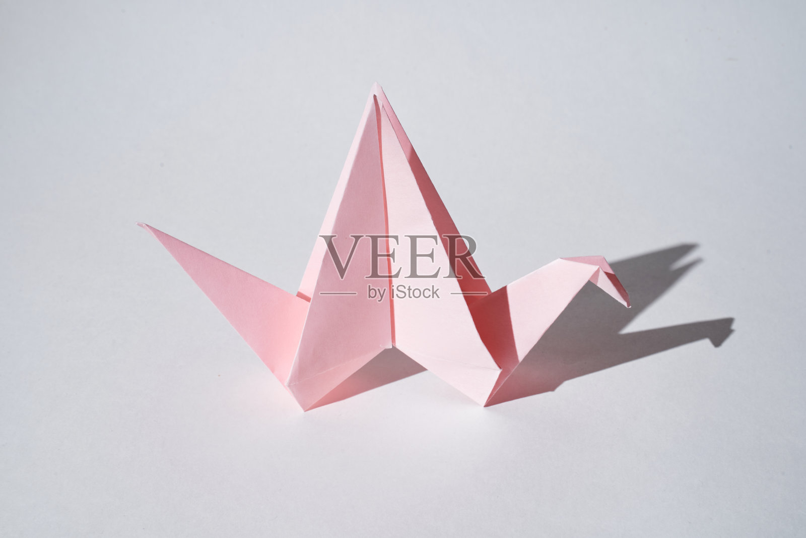 在强光下，白色的背景上立着粉红色的纸龙雕像。照片摄影图片