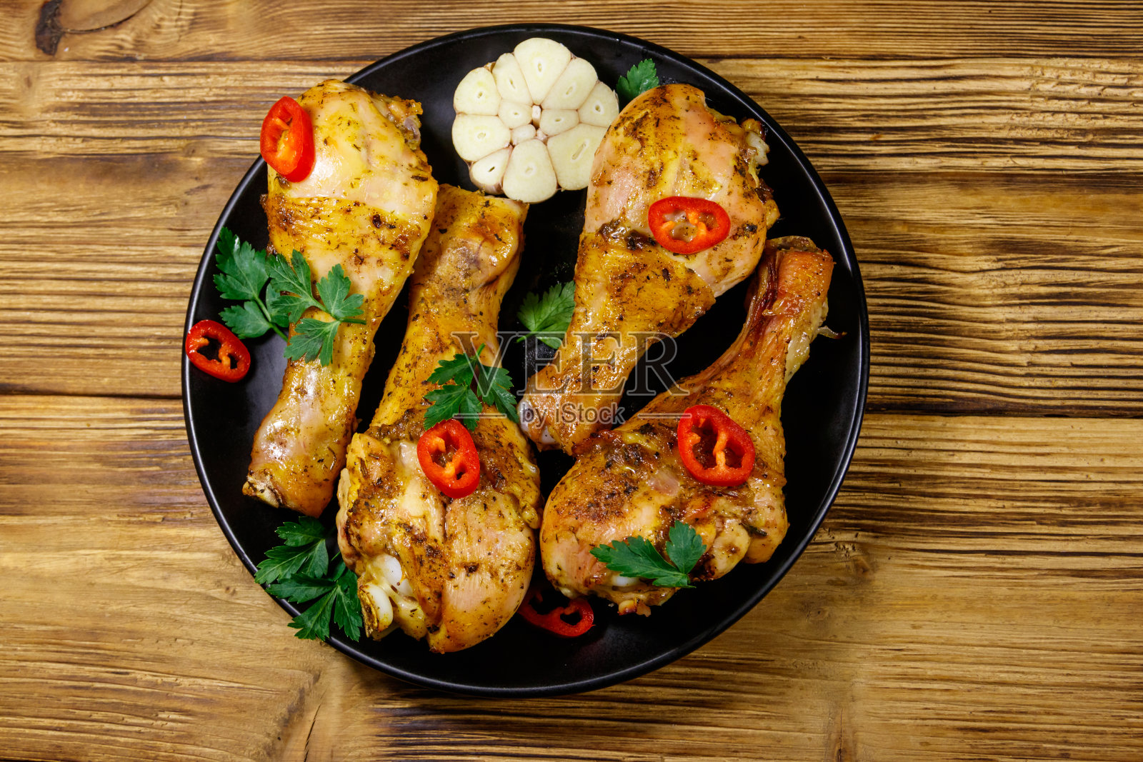 木桌上的黑盘子里放着烤鸡腿和香料。俯视图照片摄影图片