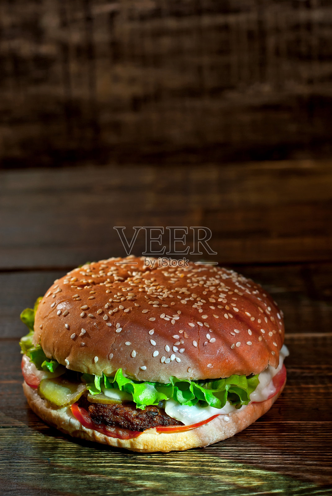 汉堡放在深色木板上。芝士汉堡与肉排和香草在黑色的背景。食物与鲜明的灯光对比。文本的空闲空间。照片摄影图片