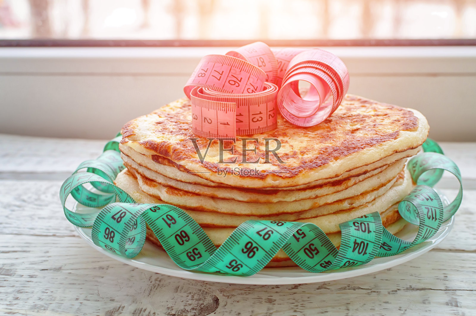 木桌上放着一叠薄煎饼，上面放着一厘米长的胶带。不健康生活方式的概念。超重。照片摄影图片