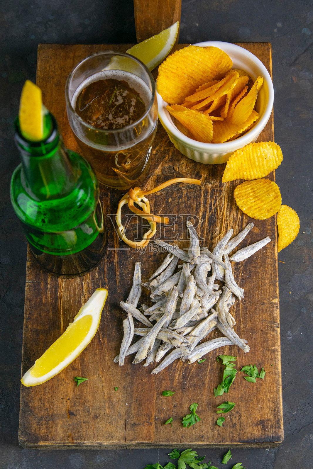 干盐渍凤尾鱼，啤酒，柠檬和薯片放在深色木板上。吃鱼时喝啤酒。特写镜头照片摄影图片