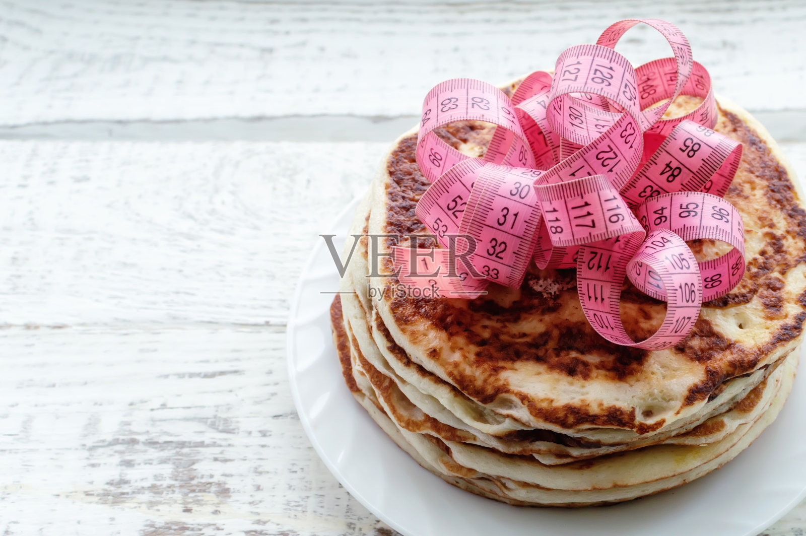 木桌上放着一叠薄煎饼，上面放着一厘米长的胶带。不健康生活方式的概念。超重。照片摄影图片