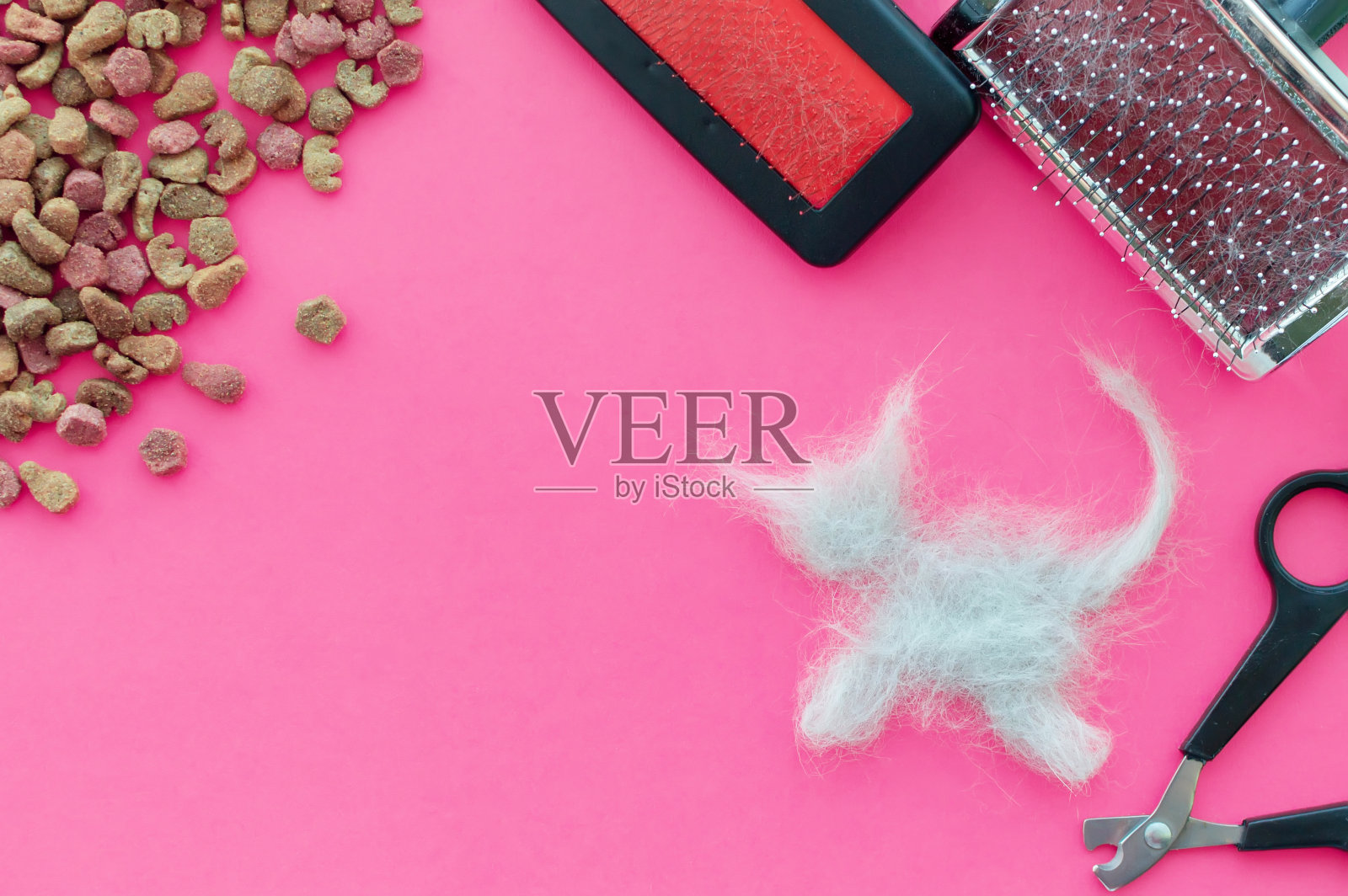 梳子，食物和剪子后剪下的猫和一块猫毛形状的粉红色背景上的猫。从上往下看。照片摄影图片