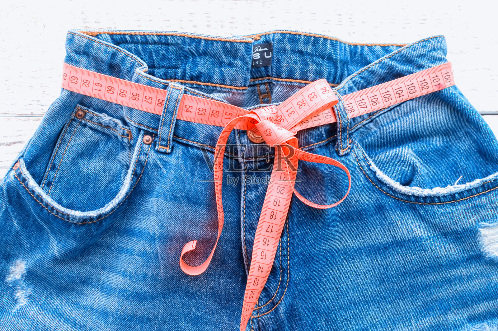 粗斜纹棉布裤子，木质背景。蓝色牛仔裤用的是卷尺而不是皮带。裤腰上系着卷尺的牛仔裤。健康的生活方式和饮食的概念。照片摄影图片