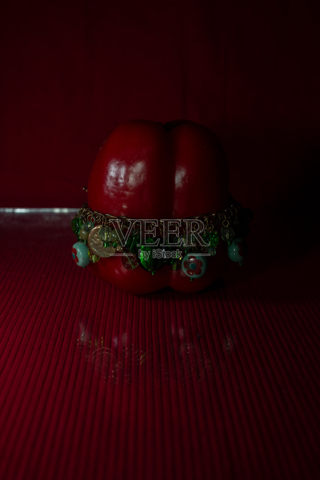红色灯笼椒上戴着一个不寻常的手镯。反射在玻璃上。红色的背景照片摄影图片
