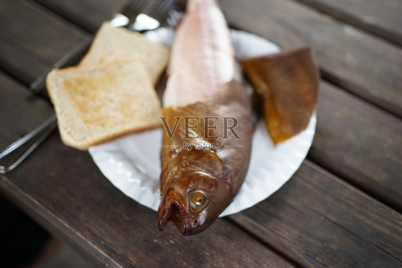 近距离的烟熏鳟鱼在一个盘子与吐司和刀叉在一个木桌照片摄影图片
