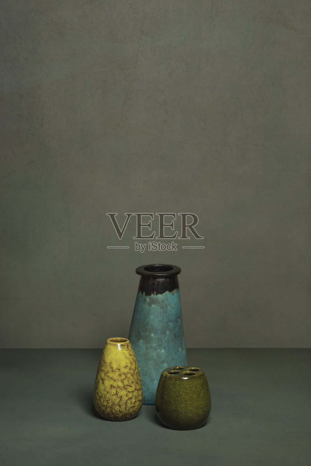 灰色墙壁前的灰色桌子上放着一个蓝色、黄色和绿色的古董花瓶。照片摄影图片