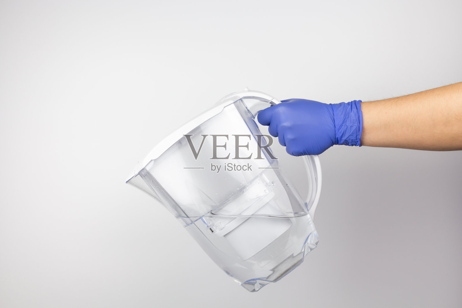 戴着防护手套，手持一个白色背景上有过滤器的塑料水壶照片摄影图片