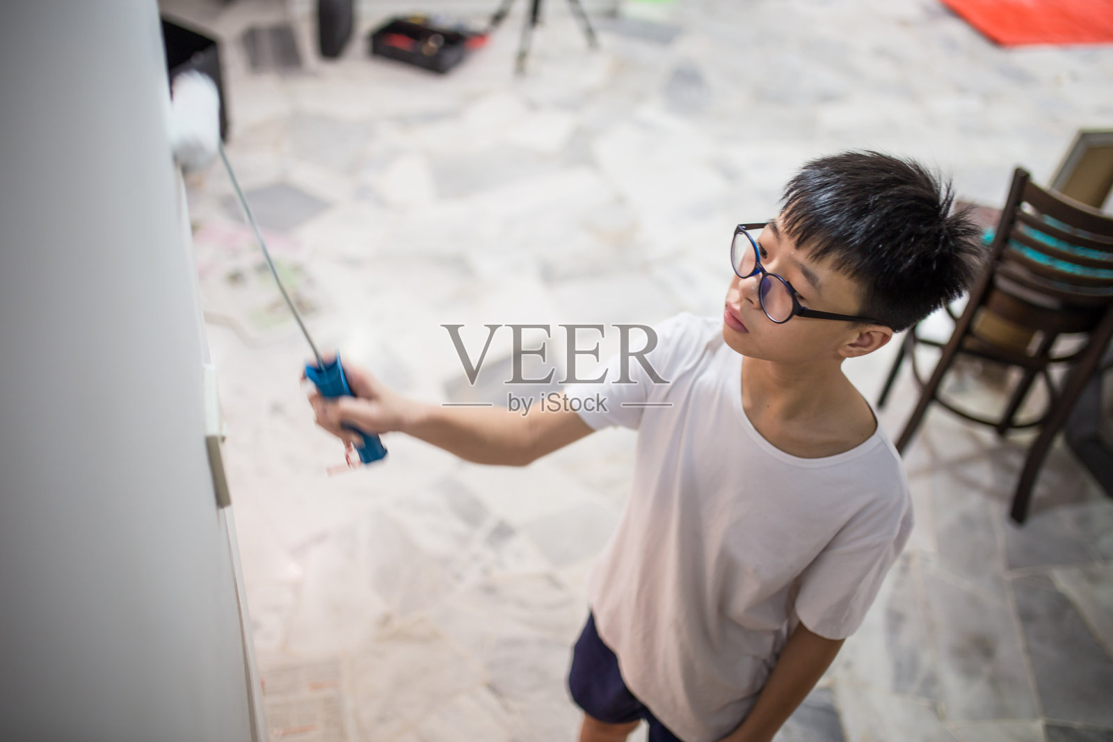 一位亚洲青少年正在用油漆滚筒帮助家庭粉刷他们的新房子照片摄影图片