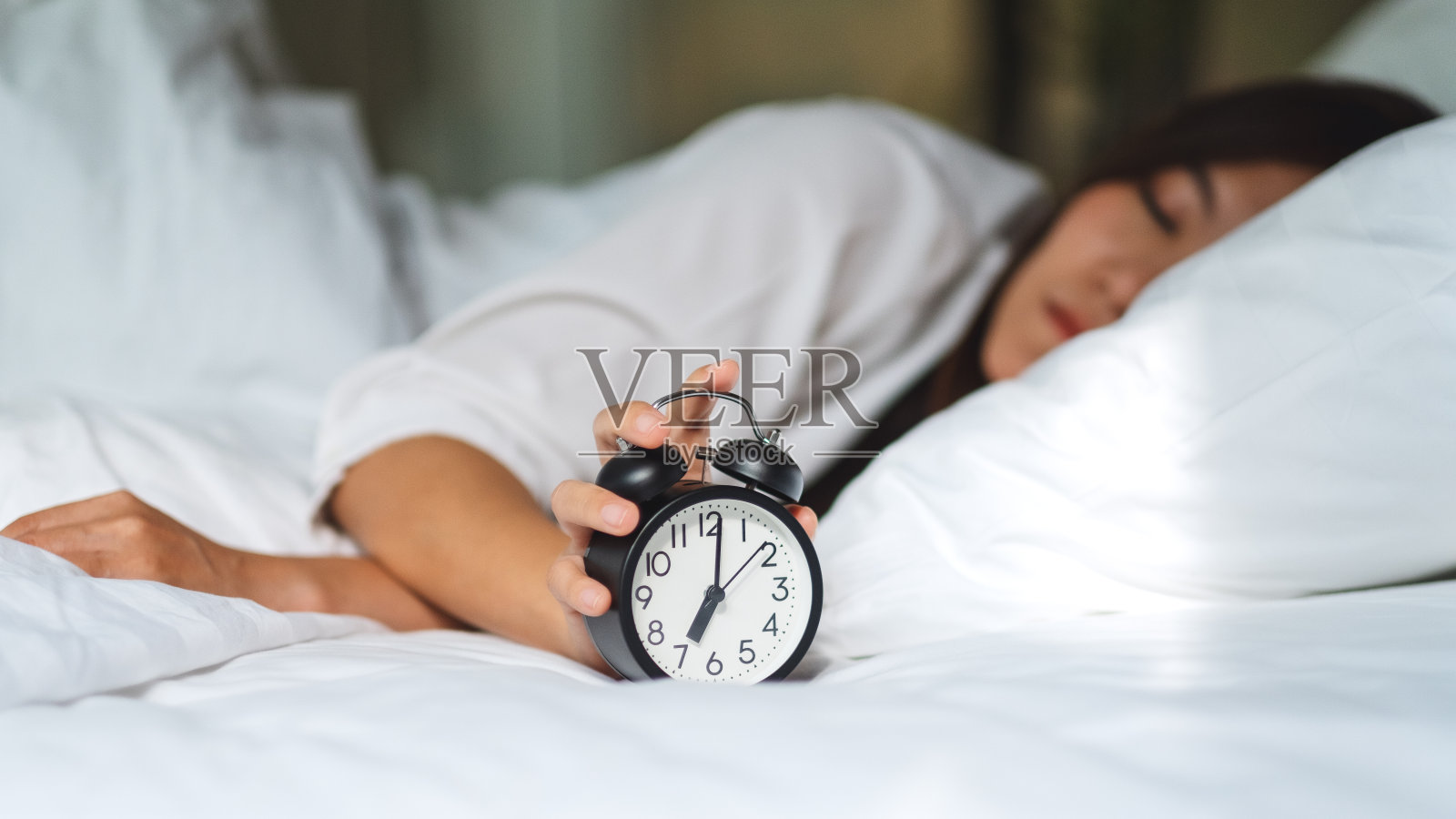 一名女子，早上睡在舒适的白色床上，却关掉了闹钟照片摄影图片