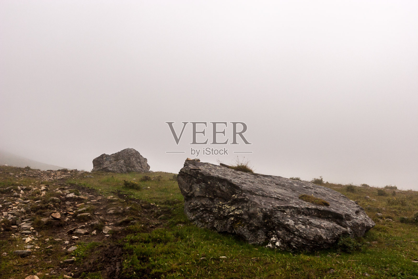 山腰上有几块大石头，背景是雾。地上有绿色的草。岩石小道。副本的空间。水平的。照片摄影图片