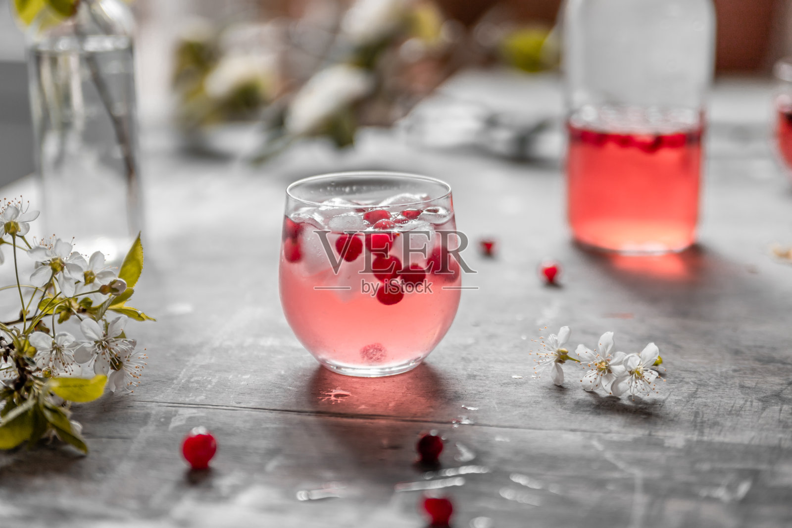 灰色破旧的桌子上放着一杯加冰和浆果的蔓越莓柠檬水，桌上放着花和叶子。照片摄影图片