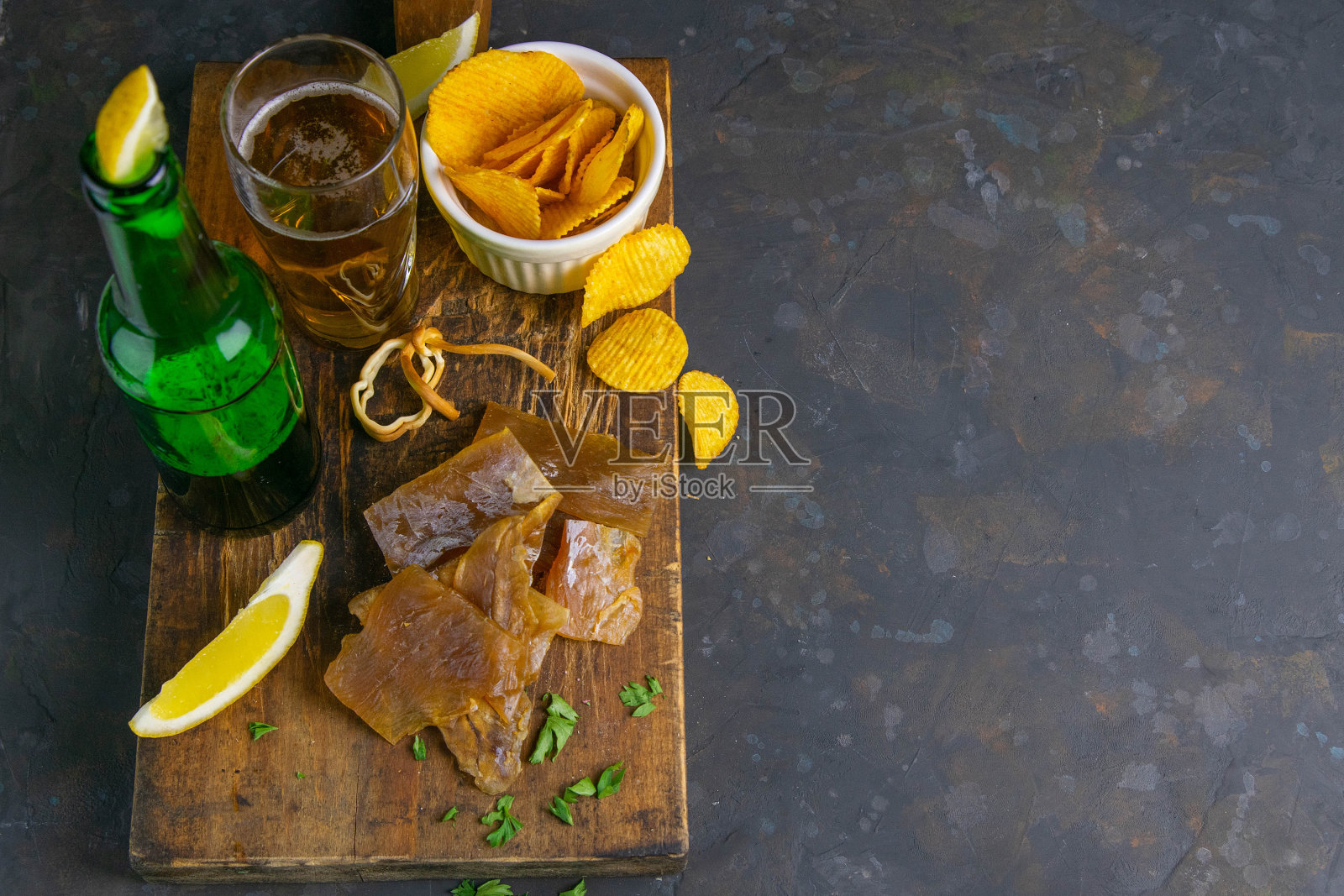 干鲶鱼片配啤酒，柠檬和薯片放在深色木板上。吃鱼时喝啤酒。顶部视野与清晰的空间照片摄影图片