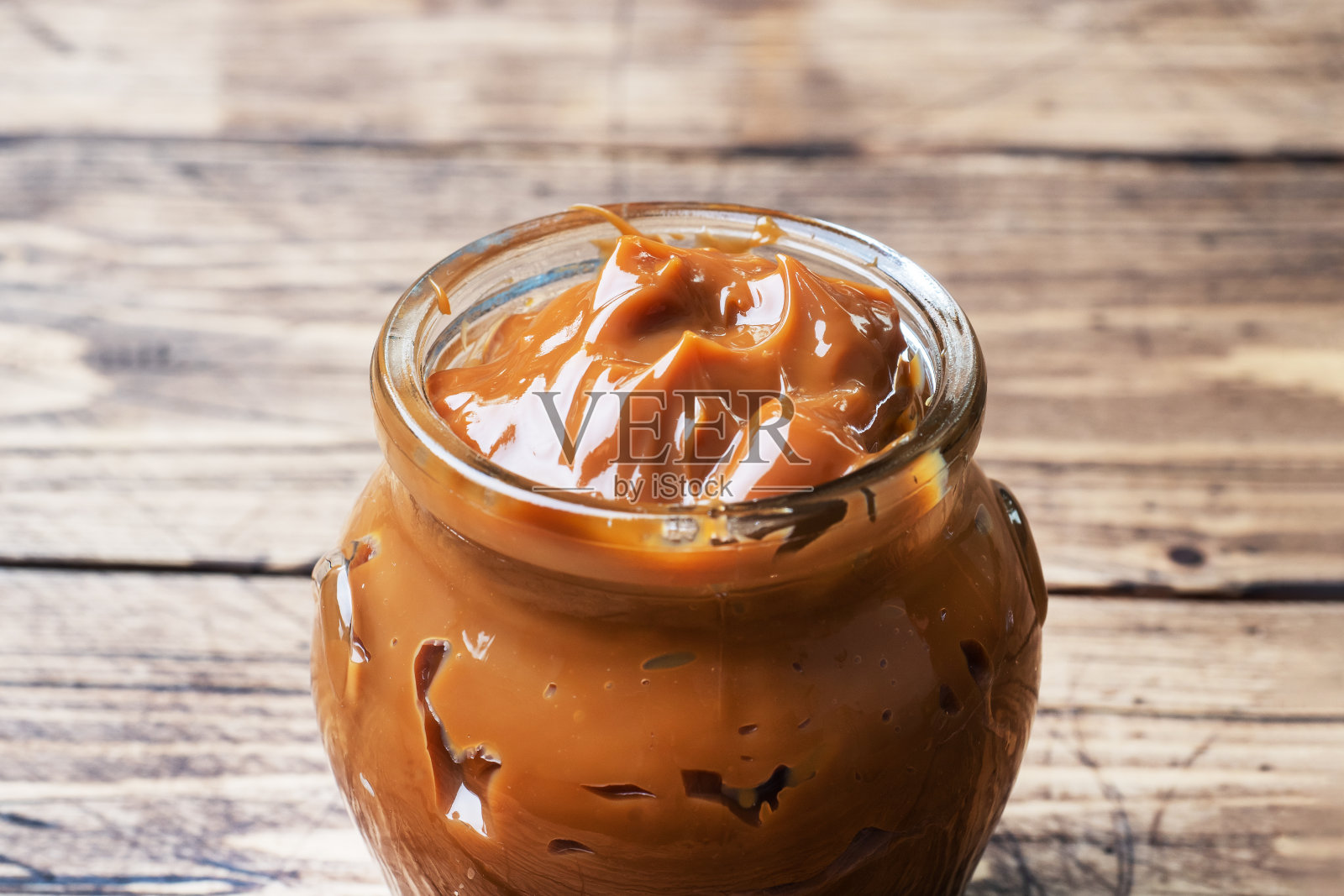 木质背景上放着一个玻璃罐的煮炼乳。早餐和甜点的甜意面。副本的空间。照片摄影图片